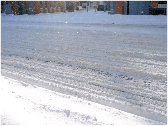 ブラックアイスバーンの上に積雪した道路(手前は歩道に積もった雪)