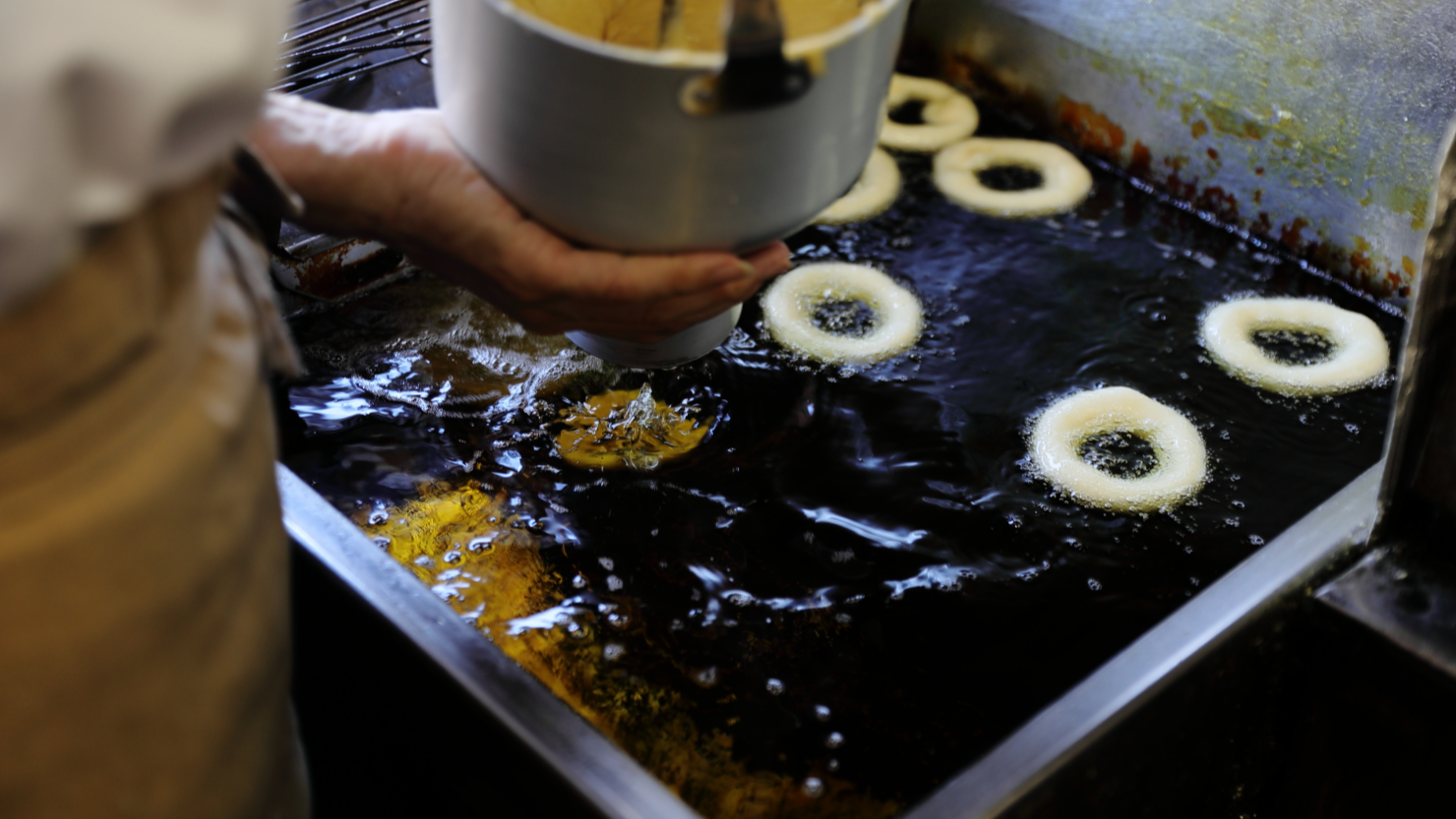 生地を詰めたドーナツマシーンを使い、一つずつフライヤーで揚げていく