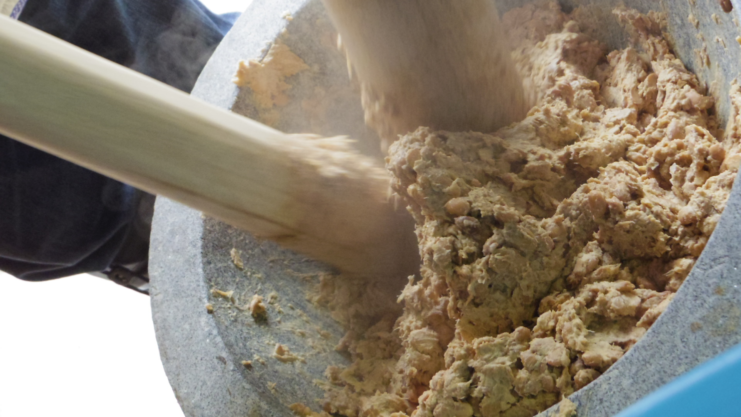 杵と臼を使って大豆をつぶす様子