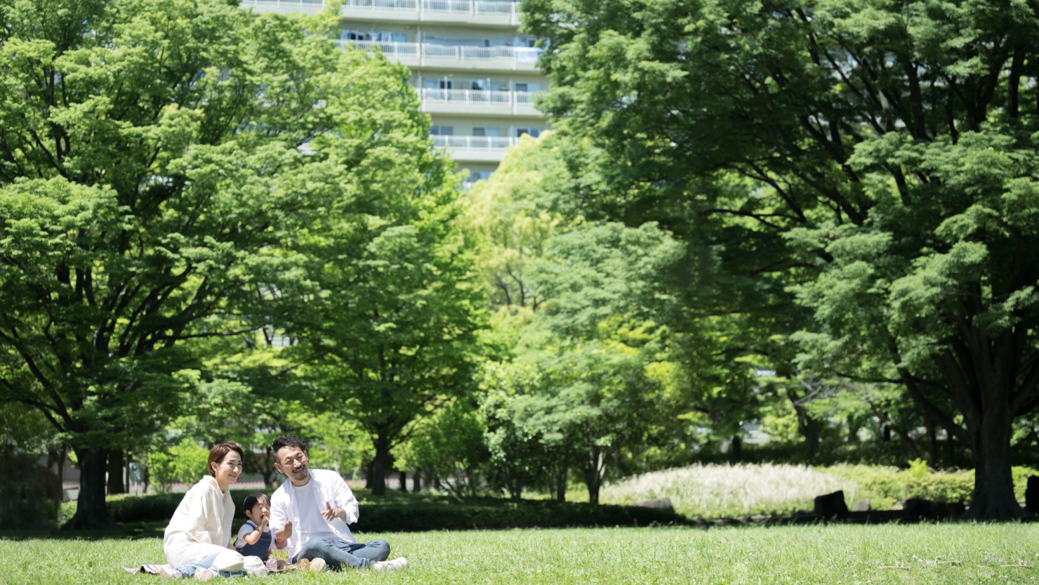 引越し先の新緑の公園でくつろぐ家族のイメージ