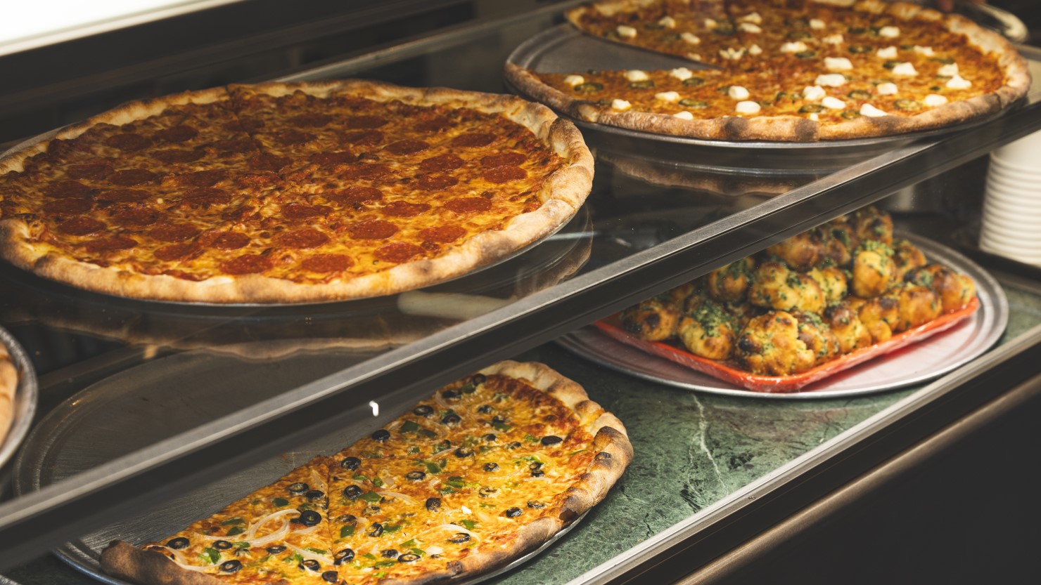 定番のピザはチーズ、ペパロニ、クリームチーズハラペーニョの3種、Weekly Specialのピザ2種がショーケースに並びます。1スライス450円〜。ガーリックノットやポテト、クラムチャウダーなどのサイドメニューも充実。テイクアウトもできます