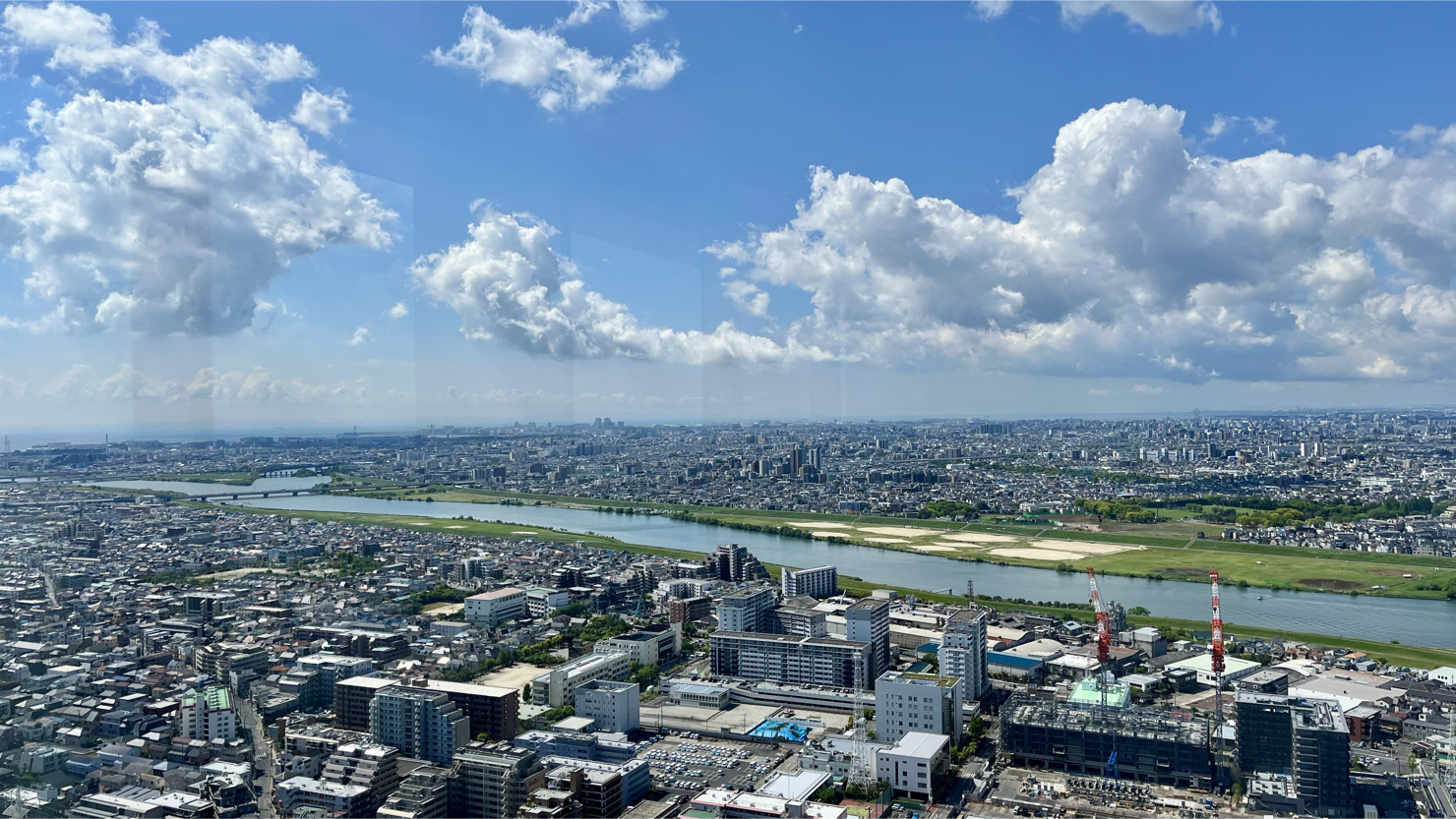 アイ・リンクタウン展望施設から駅南側を望む。河川は江戸川、写真右手前は建築工事中の「リーフシティ市川」（2025年5月撮影）