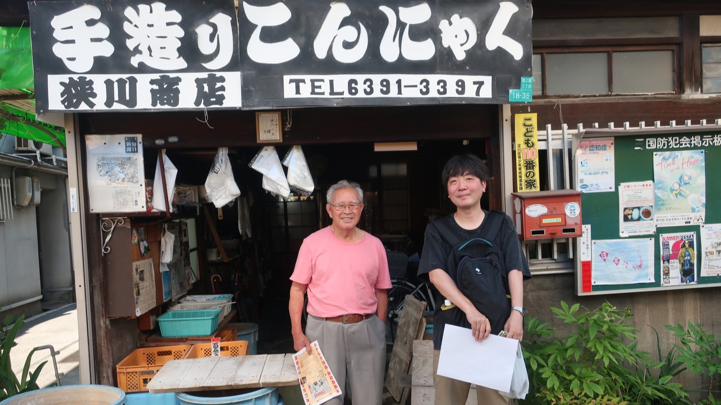 狹川一三さんと店頭で記念撮影。写真右の掲示板に貼られているのは日本原水爆被害者団体協議会の連凧