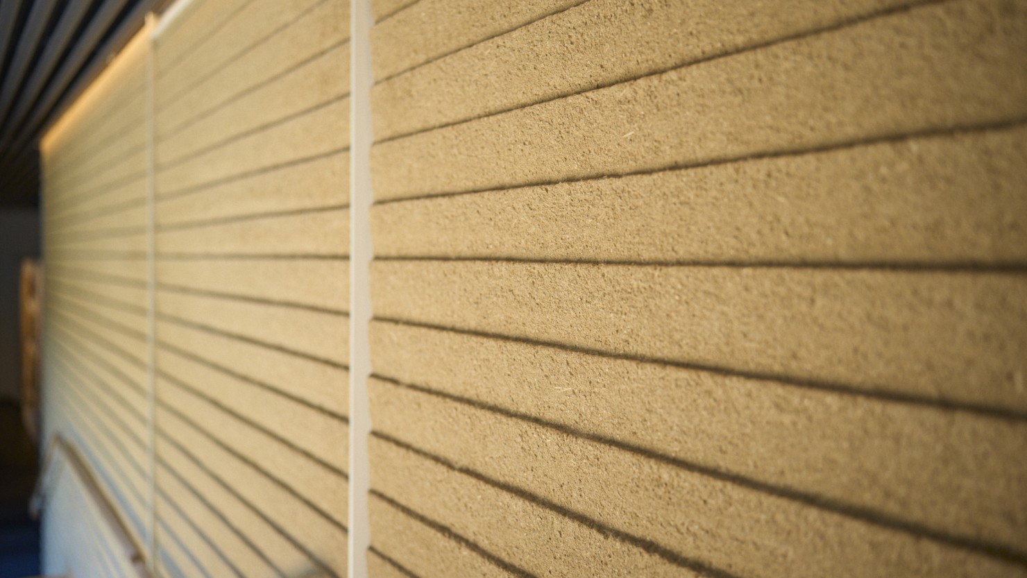 兵庫県淡路市出身の左官職人・久住有生（なおき）氏、章（あきら）氏による手仕事。お寺や神社の土壁を構成する版築（はんちく）をモチーフに、地上階の壁全面を見事に仕立てている