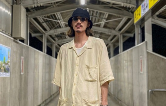 黒のバケットハットにベージュのシャツとブラックスニーカー