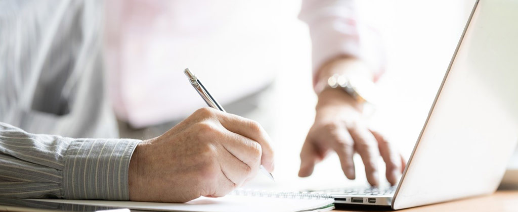 パソコンを見てメモをする男性