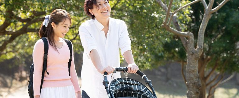 子供の乗ったベビーカーを押す男性と笑顔で話す女性