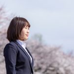 リクルートスーツを着て桜の木の下に立つ女性の写真