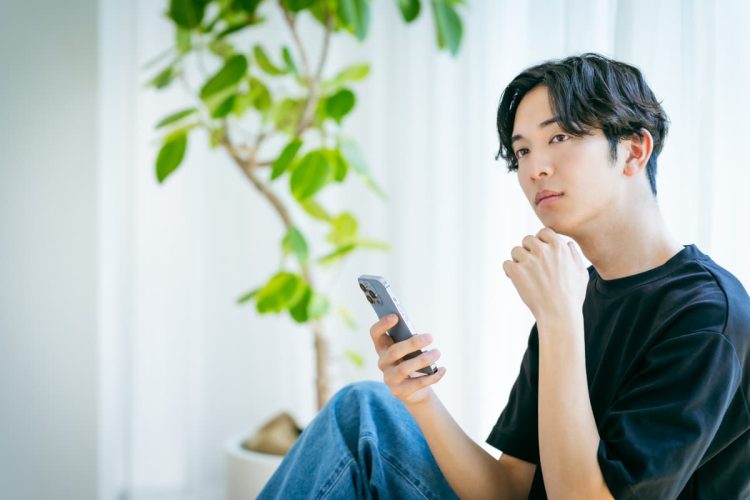 スマホを持ちながら悩む男性