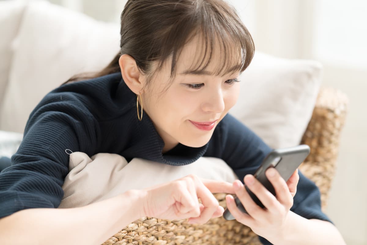 ソファにいこたわってスマホを操作する女性