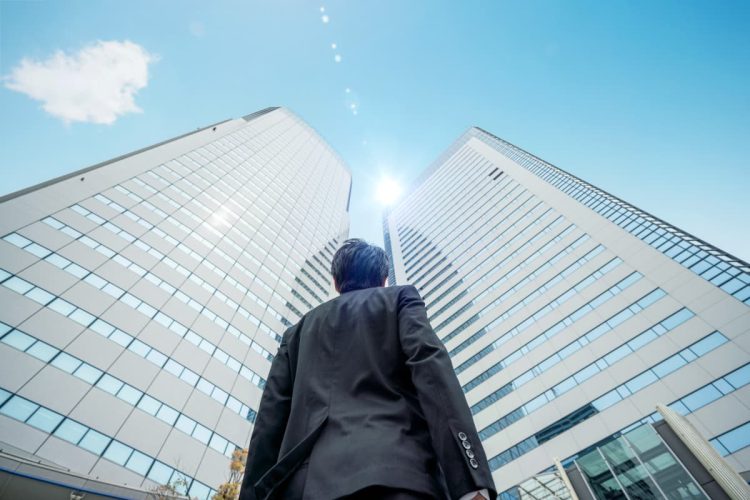 高層オフィスの前でビルを見上げるビジネスマン