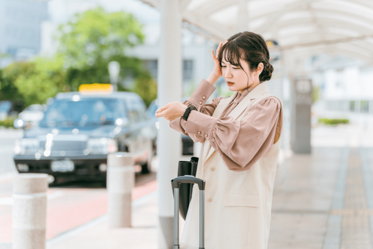 駅で腕時計を見ながら時間を確認する女性