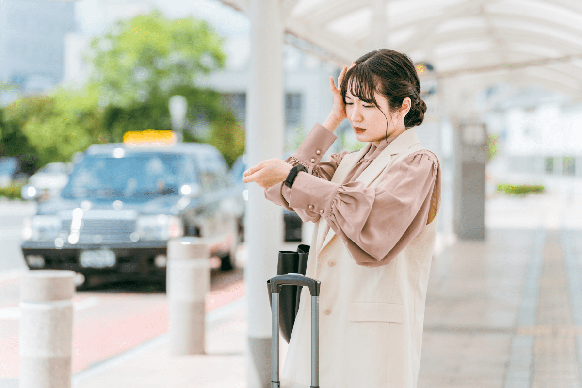 駅で腕時計を見ながら時間を確認する女性