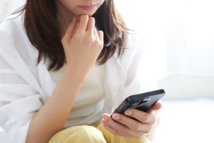 スマホを見て考え事をする女性