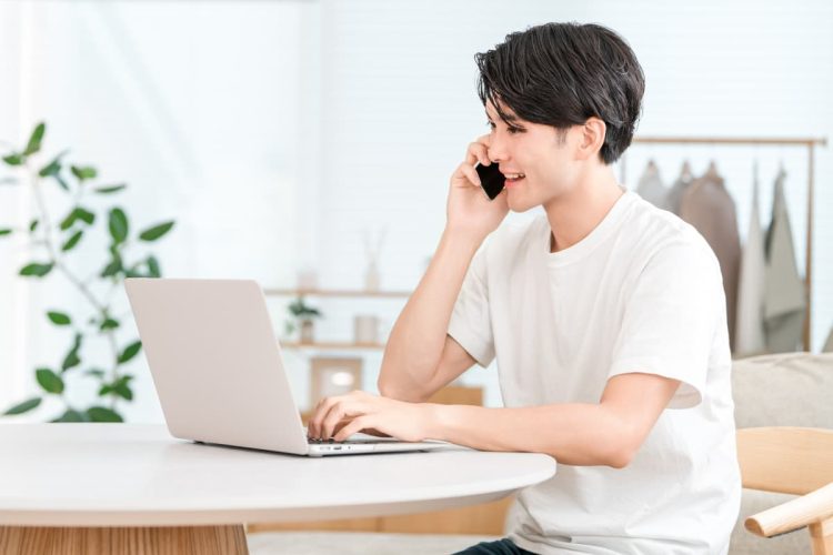 パソコンを開きながら電話をする男性