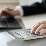 パソコンを見ながら電卓で計算する人の手