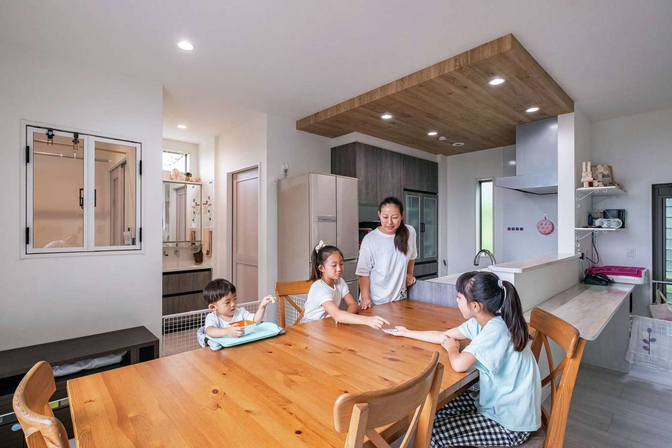 工藤建設【デザイン住宅、子育て、間取り】キッチンはおしゃれな下り天井でデザイン。横並びのダイニングは配膳しやすく片付けもラクラク。ランドリールームの室内窓を開ければ、家事をしながら家族とコミュニケーションを図れる