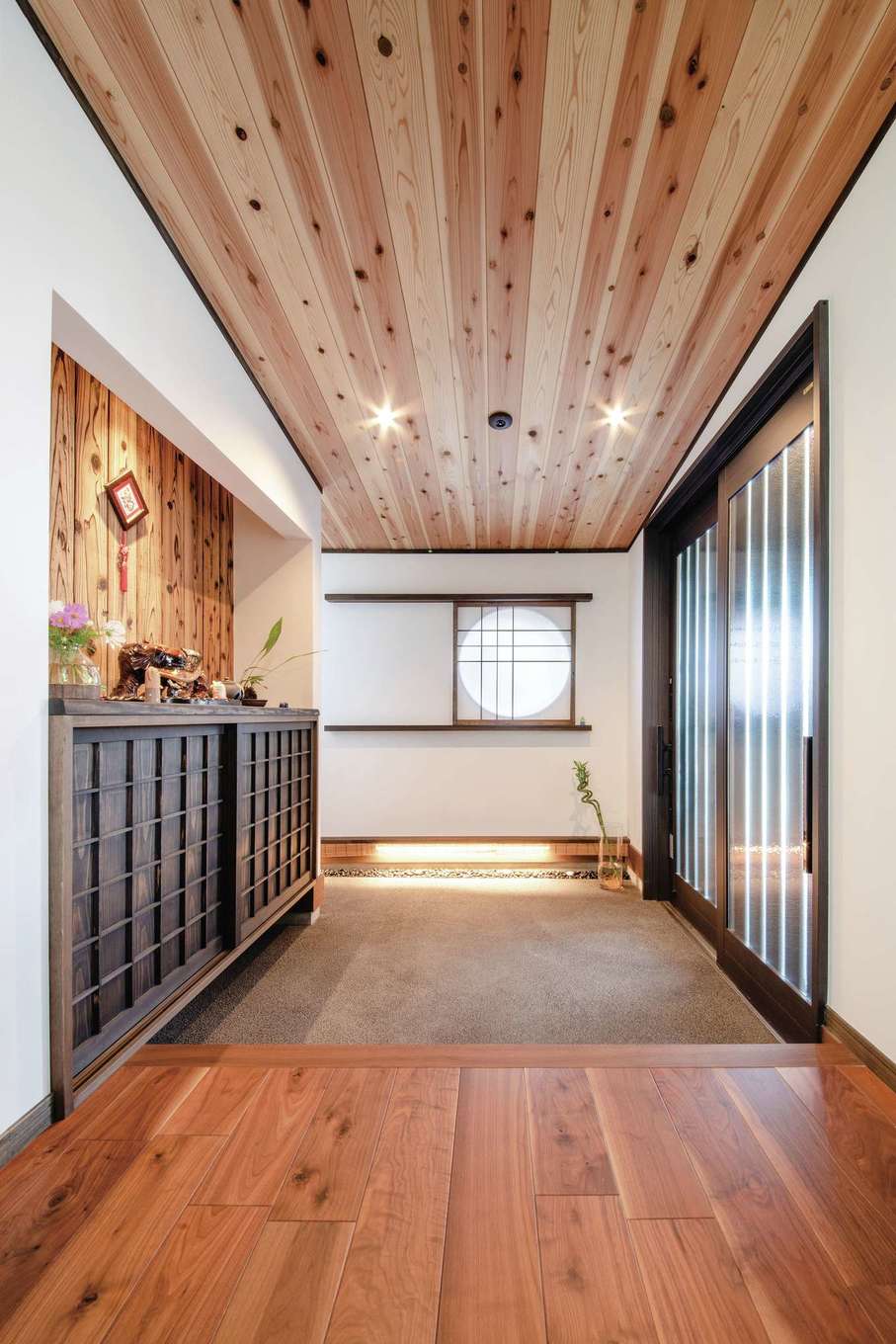 丸洋建設 ハウスオブハウス【デザイン住宅、自然素材、平屋】高級旅館を思わせる土間仕上げの玄関ホール。天井は杉、床はウォールナット、壁は焼杉。夜になると、丸窓に紅葉のシルエットが浮かび上がる