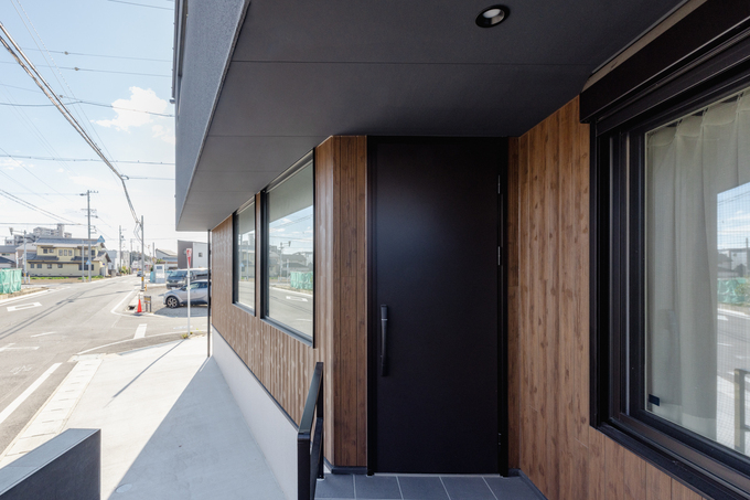 シンプルでモダンなデザインの玄関エントランス。木目調の壁とブラックの扉が、外観に上品な印象を与えている。