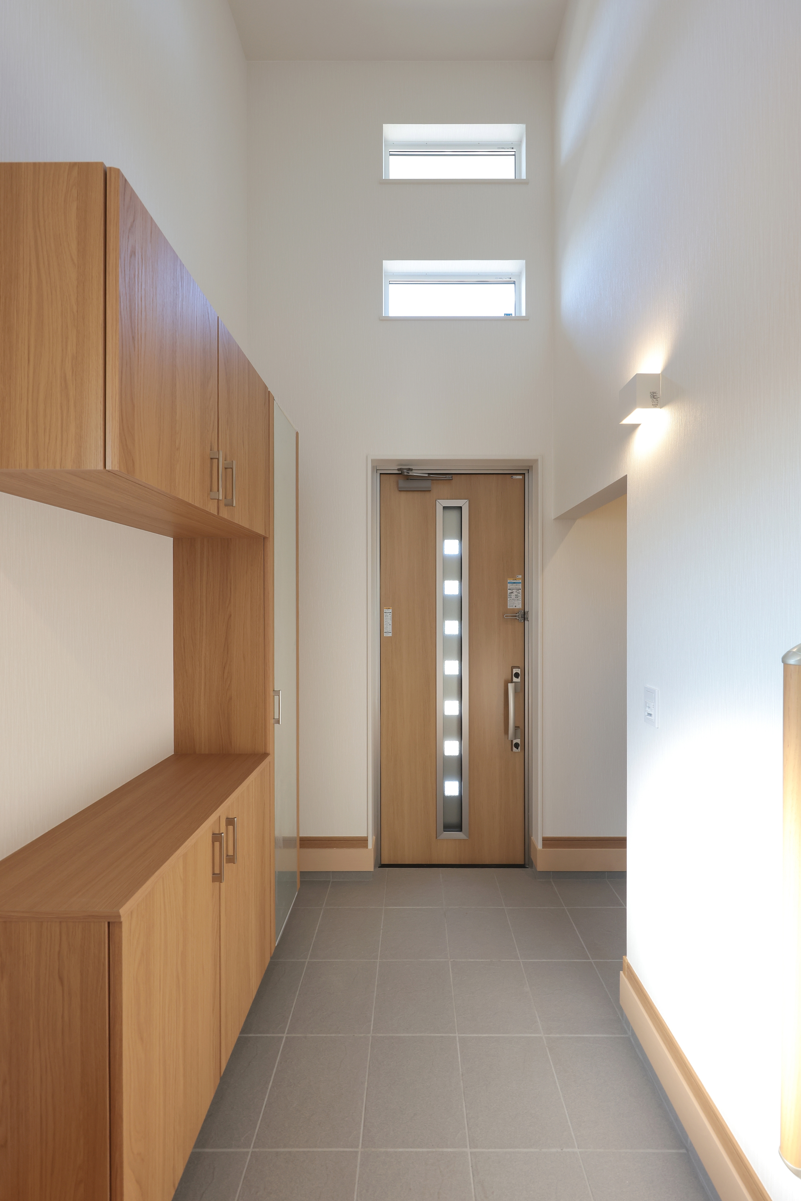 サンポウ｜木の質感が温かい玄関。明るい自然光が差し込み、シンプルで機能的なデザインが特徴的である。