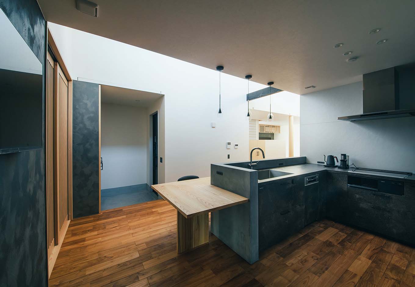 平屋建築ブルーハウス【デザイン住宅、建築家、平屋】玄関はホール無しでダイニングキッチンに直結する。無駄なスペースを省いた分、暮らしの中心となるLDKのスペースを広々と確保できた。キッチンは機能性を重視してL字型を選択。奥さまは食事の支度をしながら、帰宅した家族に「おかえり」とすぐに声かけができる。キッチンの横には和室を配置