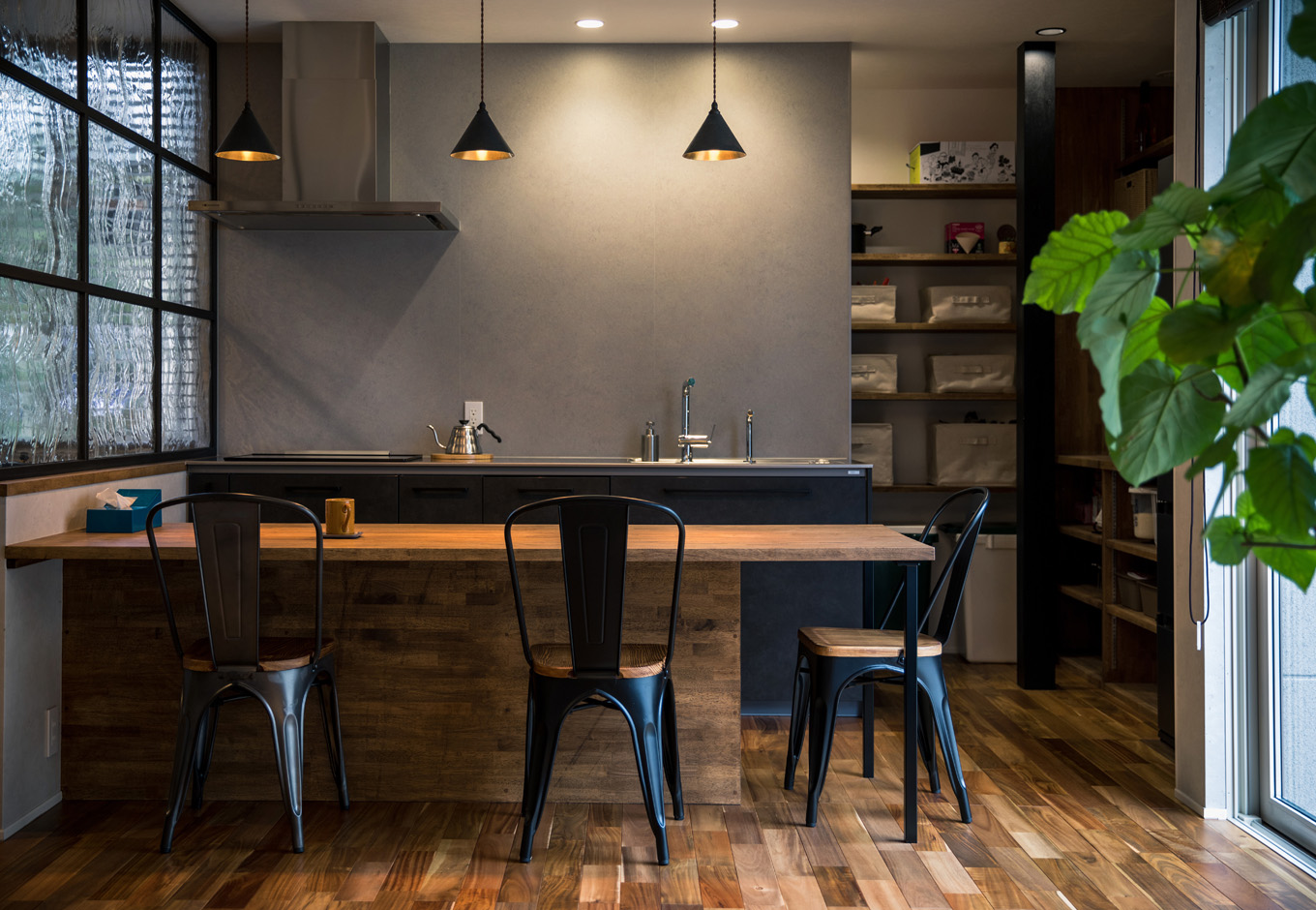 SEIEN ARCHITECT【デザイン住宅、建築家、インテリア】グレーの壁の微妙な色合いや素材感にまでこだわり、バーのように洗練されたダイニング空間が実現。黒いアイアンと無垢材が絶妙に調和し、心地よさをもたらしている