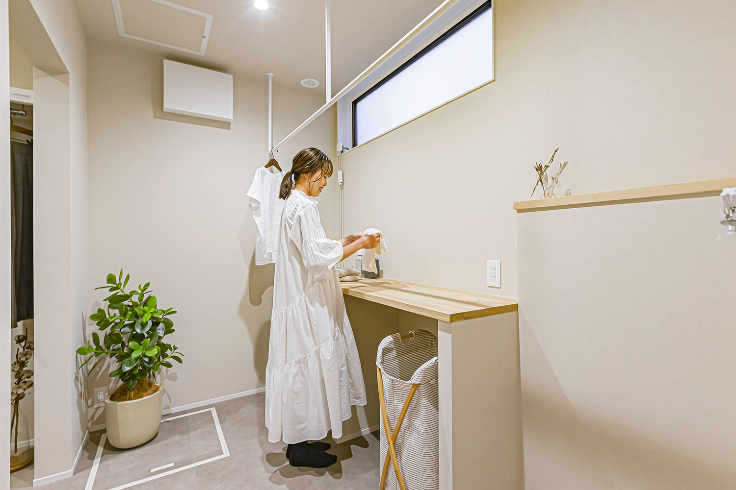 ARRCH アーチ【浜松市中央区笠井町206-5・モデルハウス】ランドリーは３畳の広さ。造作の家事カウンターでは洗濯物を畳んだり、アイロンをかけたりできる。カウンターの下には可動棚を設けてあり、しまうもののサイズに合わせて棚の高さを変えられる。ランドリーはファミリークロークと洗面スペースにつながる回遊動線上にあるため、洗濯物を干してあっても邪魔にならないように通路のスペースをしっかり確保している