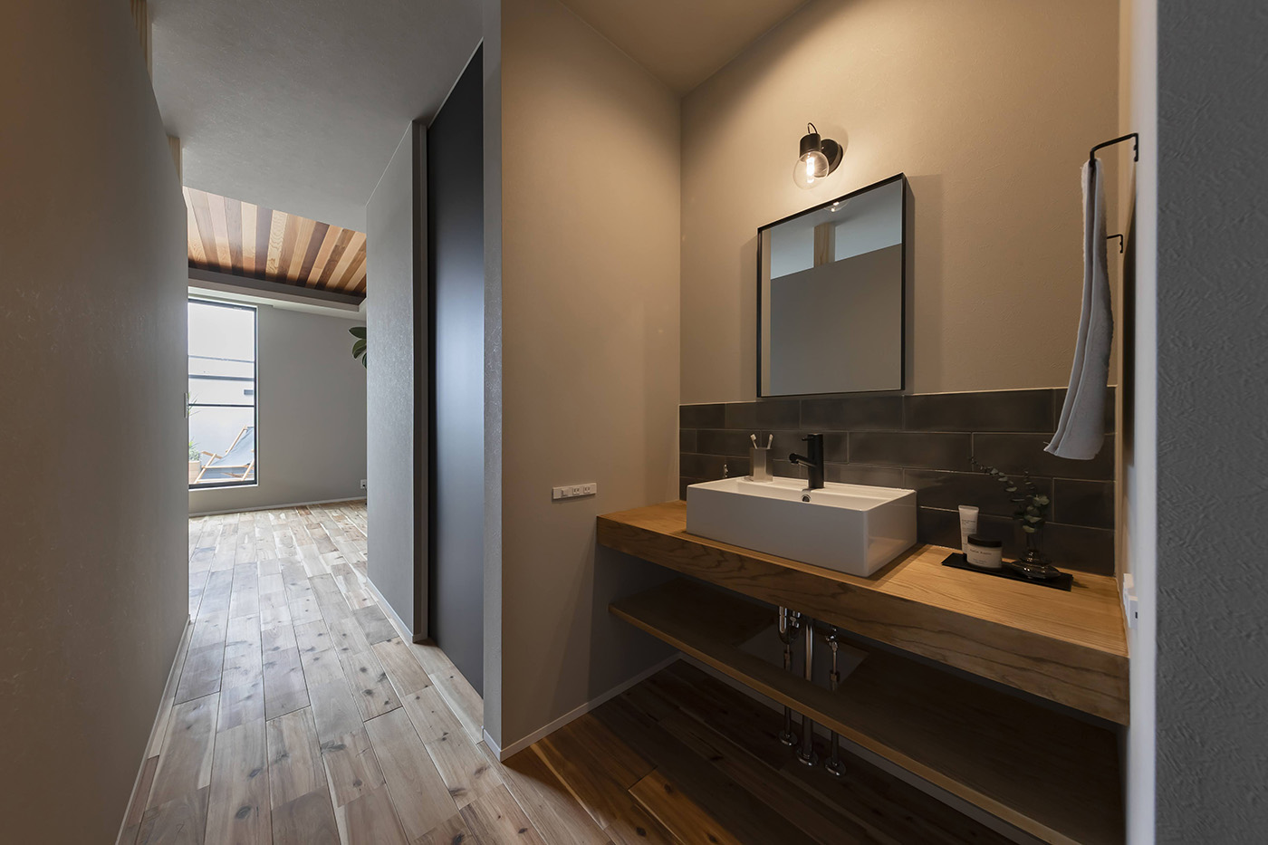 ARRCH アーチ【浜松市中央区笠井町1018-3・モデルハウス】空間を無駄なく利用し、トイレの横の壁面に設けた洗面スペース。木目のカウンターにベッセル型の洗面器を設置し、大判タイルをアクセントに用いて、洗練された雰囲気に演出。洗面スペースの隣にファミリークローゼットがあり、朝の支度もスムーズにできる