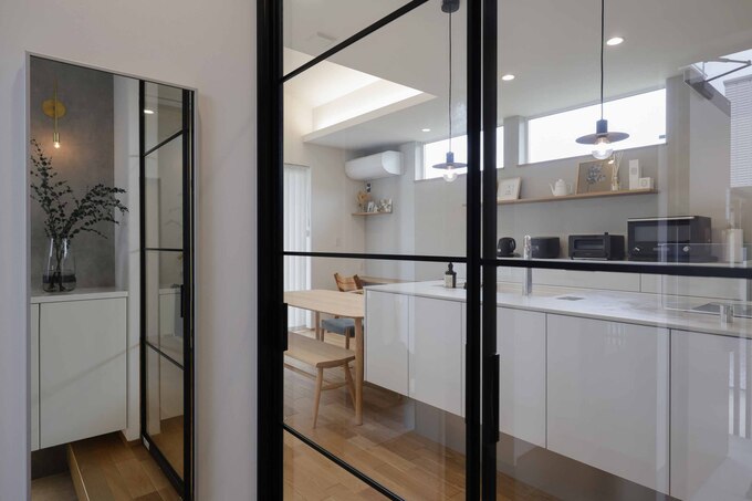 白を基調としたモダンなキッチン。大きな窓から光が入るため明るく、開放感がある。ガラス扉で空間を仕切りつつも視覚的な広がりを持たせている。