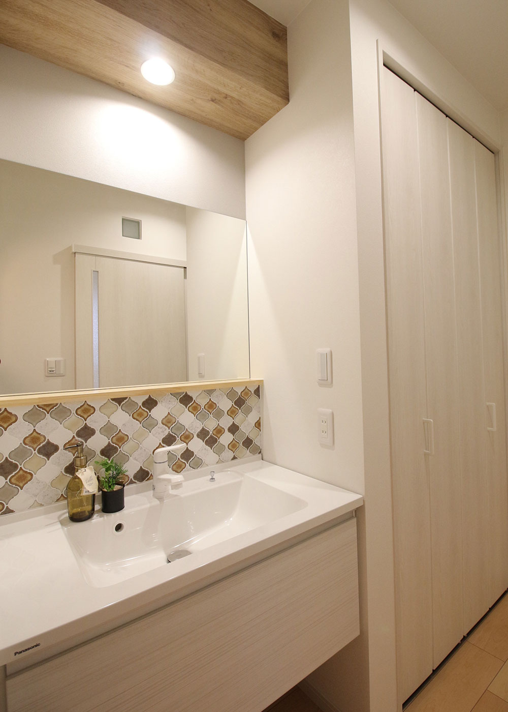 小野田産業～designers house project～【1000万円台、デザイン住宅、子育て】横一面にタイルと鏡を造作した清潔感あふれる洗面台。脱衣室・浴室へと続く廊下には、水回り品をストックできる大容量の収納も