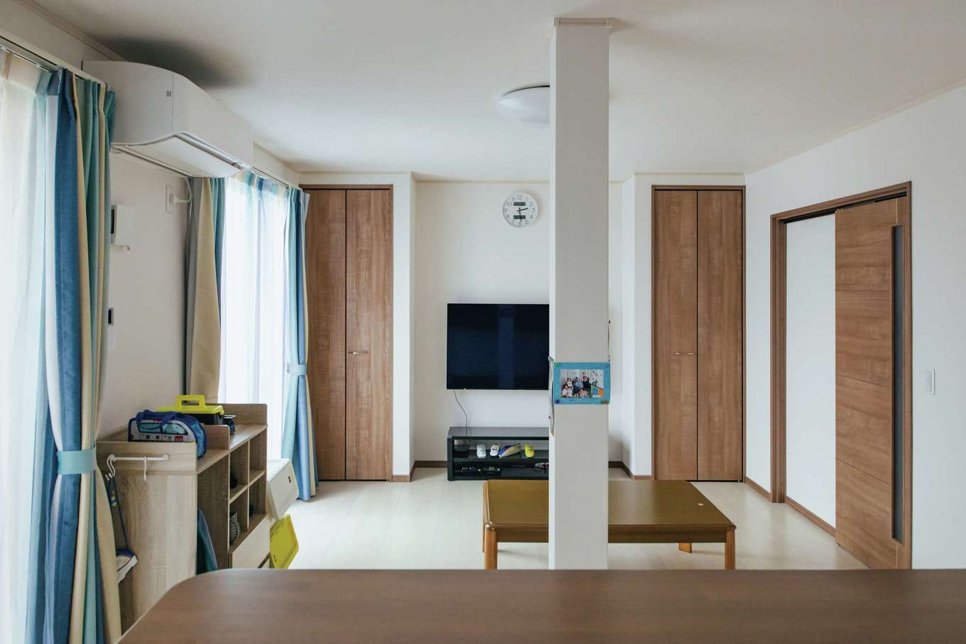 子育て安心住宅 Design Craft Office｜テレビ台の左右に用意された可動棚を備えた収納が、スッキリに貢献する。強度的に外せなかった柱は、家族の思い出のスナップを貼る場所に