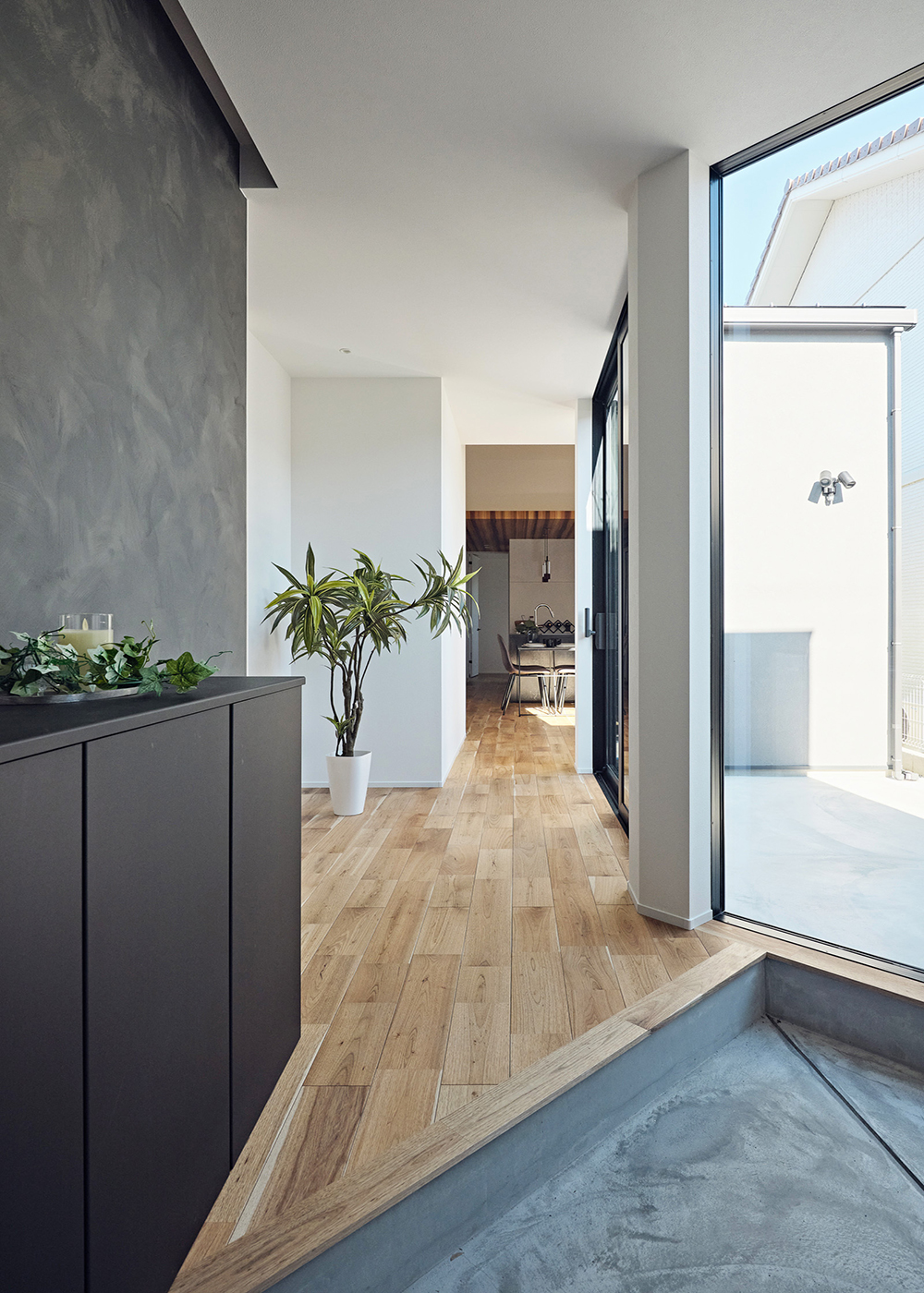 平屋建築ブルーハウス【和風、建築家、平屋】玄関にはモルタルデッキに面して大開口を設け、抜け感と開放感を強調。開口部の反対側には濃いグレーのアクセントクロスと玄関収納を設け、デザイン性へのこだわりを印象付けている