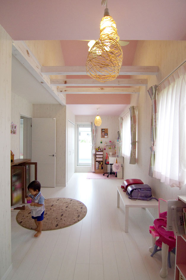住起産業（アキュラホーム三島中店）【子育て、収納力、和風】年齢も近い姉妹のお部屋。あえて空間を分けず、将来壁で仕切ることもできるように、ドア、クローゼット、窓、バルコニーへの出入りも同じように対である。屋根の形状に合わせて天井を高くし、梁を活かした空間に仕上がっている。梁はご主人がペイント。ピンク×ホワイトの空間が女の子の心をくすぐる