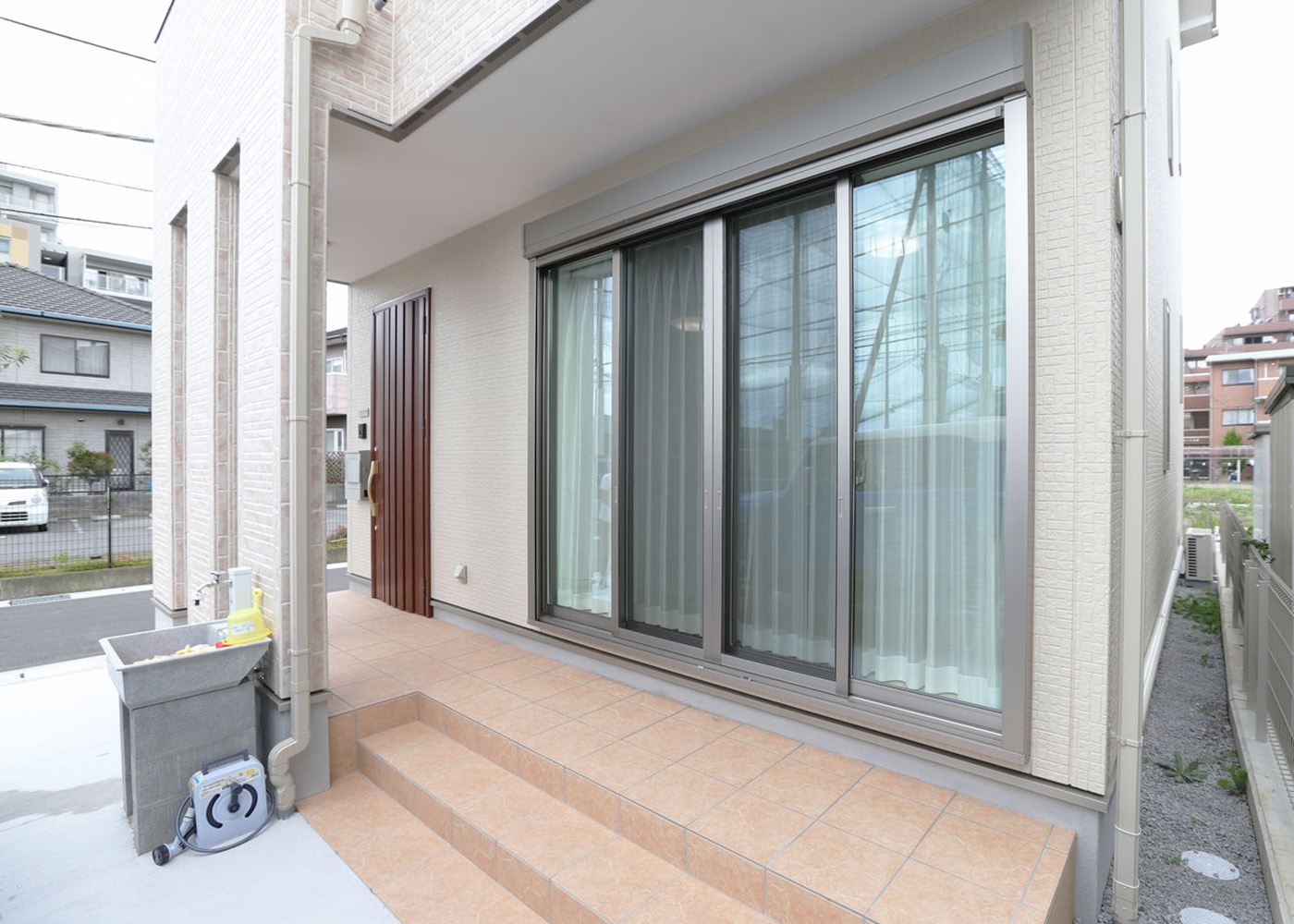 アイダ設計　山梨【デザイン住宅、狭小住宅、間取り】玄関ポーチから続くテラス。大窓を開ければリビングともつながり、いっそう開放的な空間に。目の前に駐車場があるため大きな買い物も運び入れやすく、車は程よい目隠しにも