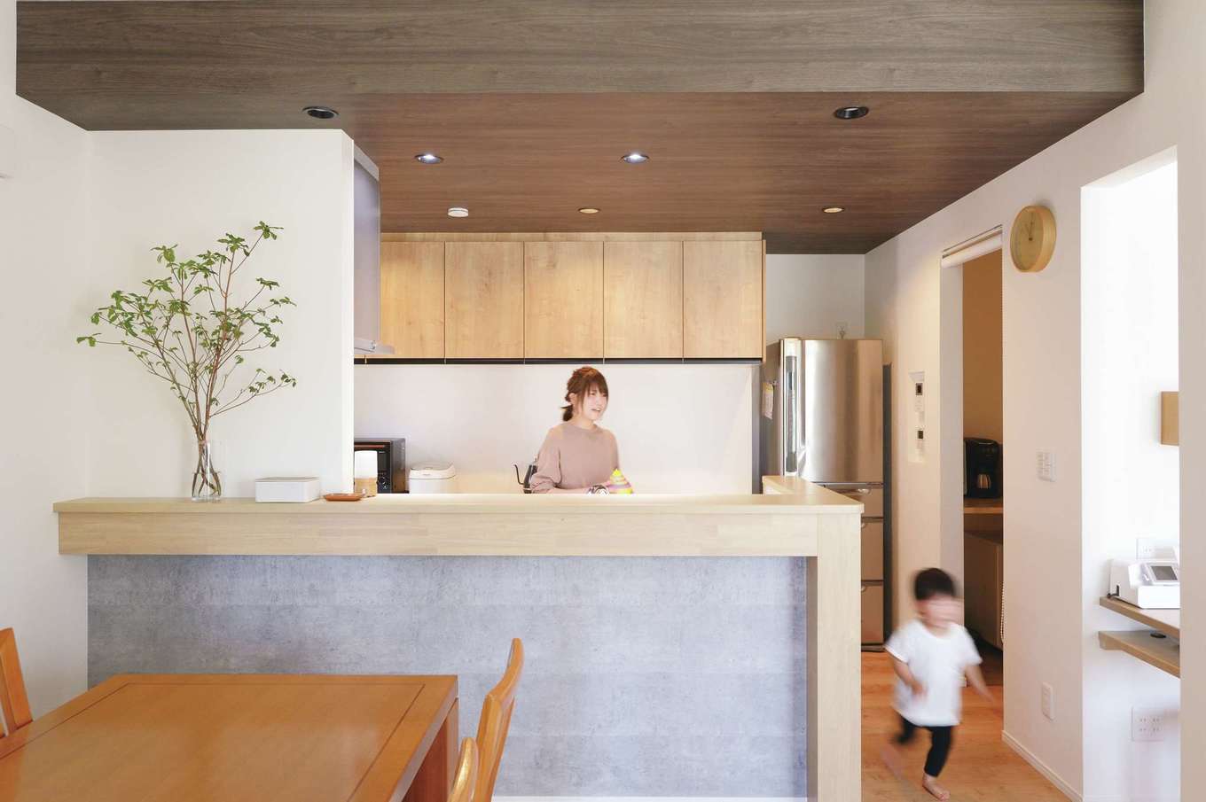 丸昇彦坂建設【デザイン住宅、子育て、間取り】対面キッチンは腰壁を高めに設定し、作業の手元がダイニングから見えないように配慮されている。腰壁のグレーとカウンターのベージュ、天井の茶色のカラーコーディネートが絶妙にマッチ