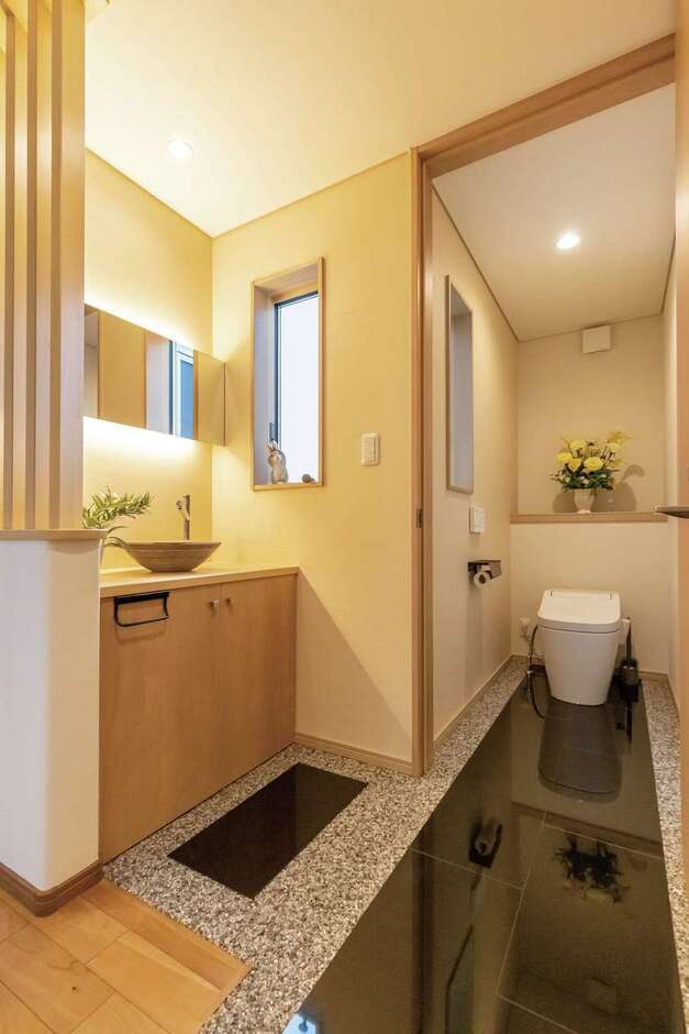 黒御影石の長い踏み込みが高級感を演出するトイレ。手洗いコーナーは角度をつけた木製ルーバーで柔らかく目隠しを