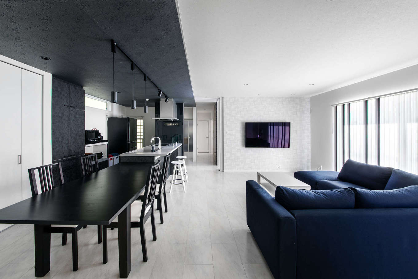 吉川住建【子育て、省エネ、ガレージ】リビングを白、キッチンを黒でコーディネートし、メリハリを利かせたモノトーンのLDK。テクノストラクチャー工法により、柱や壁のない25畳の大空間・大開口を実現した。家具、家電も『吉川住建』が空間に合わせてプロデュース