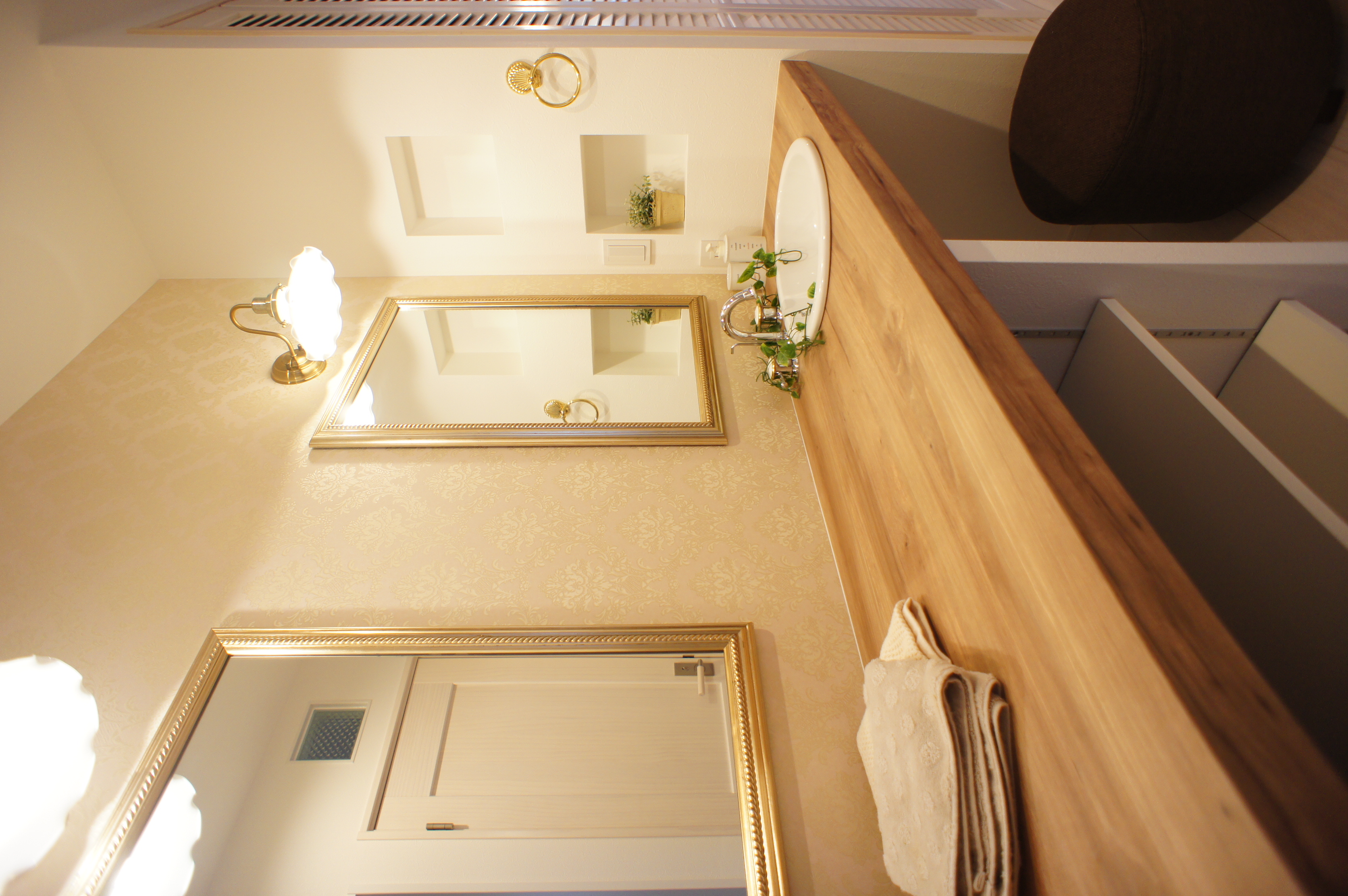 小野田産業～designers house project～｜木製のカウンターが温かみを感じさせる洗面スペース。ゴールドのフレームが施された鏡が、上品で洗練された雰囲気を演出している。