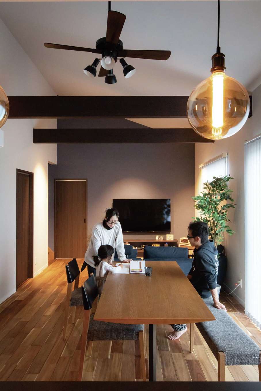 Yamaguchi Design 【自然素材、平屋、ガレージ】室内には、床下から家全体を暖めて快適な室温をキープする全館空調システム「床暖冬涼夏」を採用。勾配天井のLDKでのびのびと過ごす時間が家族のお気に入り。アクセントクロスは、同社のモデルハウスを見て「これと同じ色で」と指定した。太い梁の裏側に間接照明を仕込んだのも夫妻のアイデア