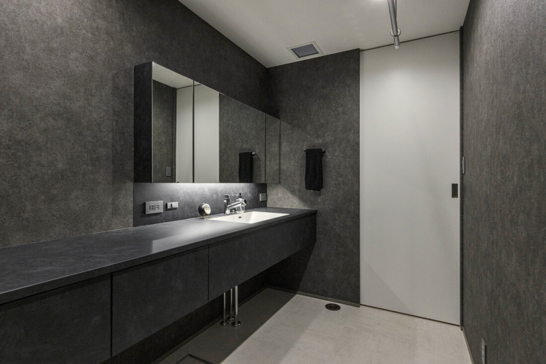 チェックハウス｜モノトーンでまとめられたスタイリッシュな洗面スペース。広々としたカウンターと大きな鏡が機能性とデザイン性を兼ね備えている。