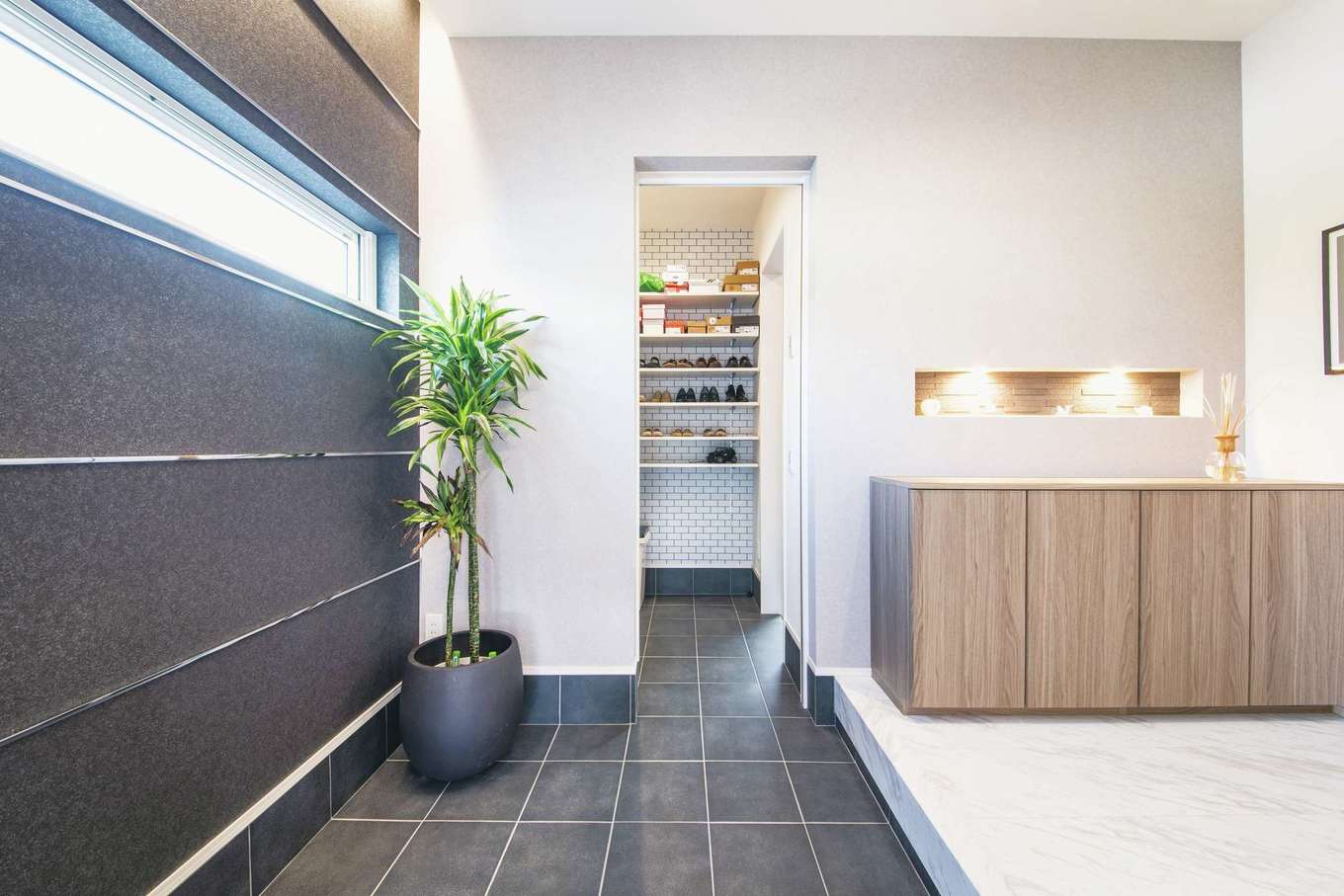 コットンハウス【デザイン住宅、子育て、省エネ】シューズクローク付きの玄関は広々としたホテルライクな空間。スチールのラインが入った黒いクロスと土間のタイルがシックに調和