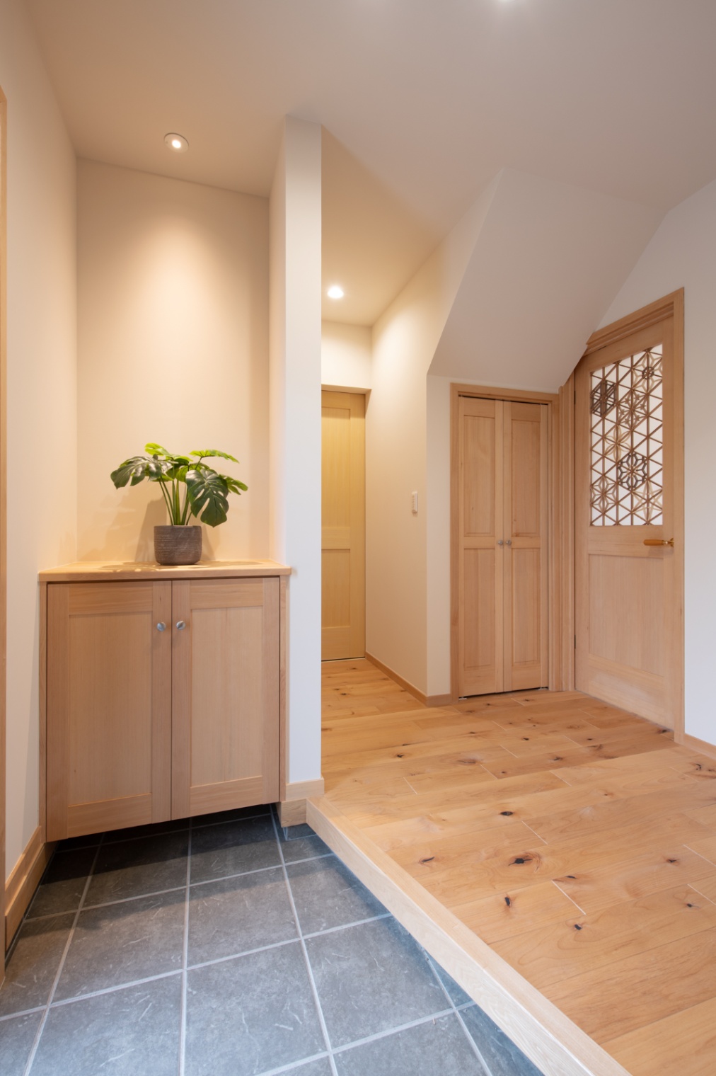 Sus∞Eco Home（サスエコホーム）｜温かみのある木材と落ち着いたトーンの玄関ホール。植物のディスプレイが柔らかい印象を与えている。シンプルながらも洗練された空間設計が特徴的である。