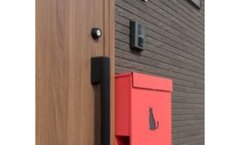 木目のドア横に赤いポストが配置された玄関。モダンなデザインが特徴で、訪れる人を温かく迎える印象を与える。