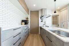 タイル調のクロスでアクセントをつけたキッチン。ドアの奥のパントリーは玄関に通り抜けでき、買い物帰りに荷物を運び込むのもスムーズ