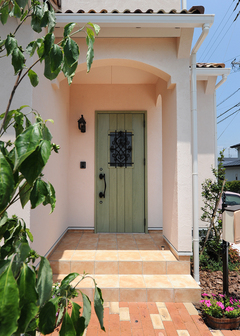 垂れ壁をRにくりぬいたエントランス、オリーブ色の玄関ドアがバランス良く調和したファサード