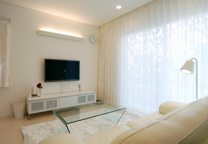 天井から床まで全面にかかるカーテンが一際印象深いリビング。間接照明や統一感のある白い家具でお洒落なインテリアにまとめた