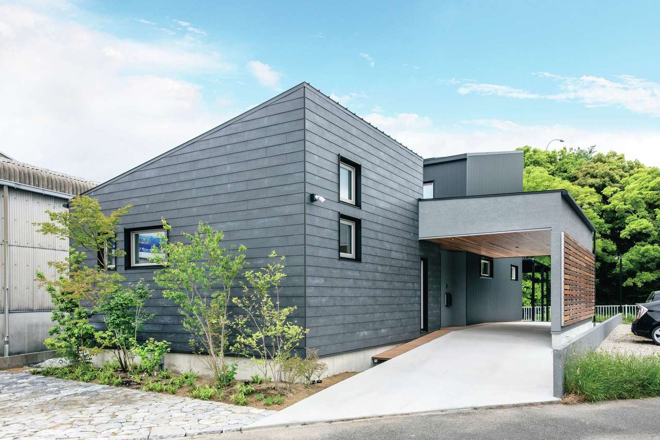 ainoa.life くらはし建築【デザイン住宅、間取り、インテリア】屋根付きのエントランスがある角張ったフォルムがクールな外観。濃いグレーのガルバリウム鋼板で外壁を統一し、ガレージの天井を板張りにしてアクセントをつけた