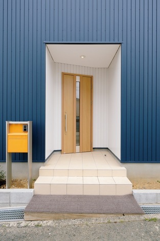 玄関ポーチはドアの壁面を斜めにして個性的に。黄色のポストがアクセント