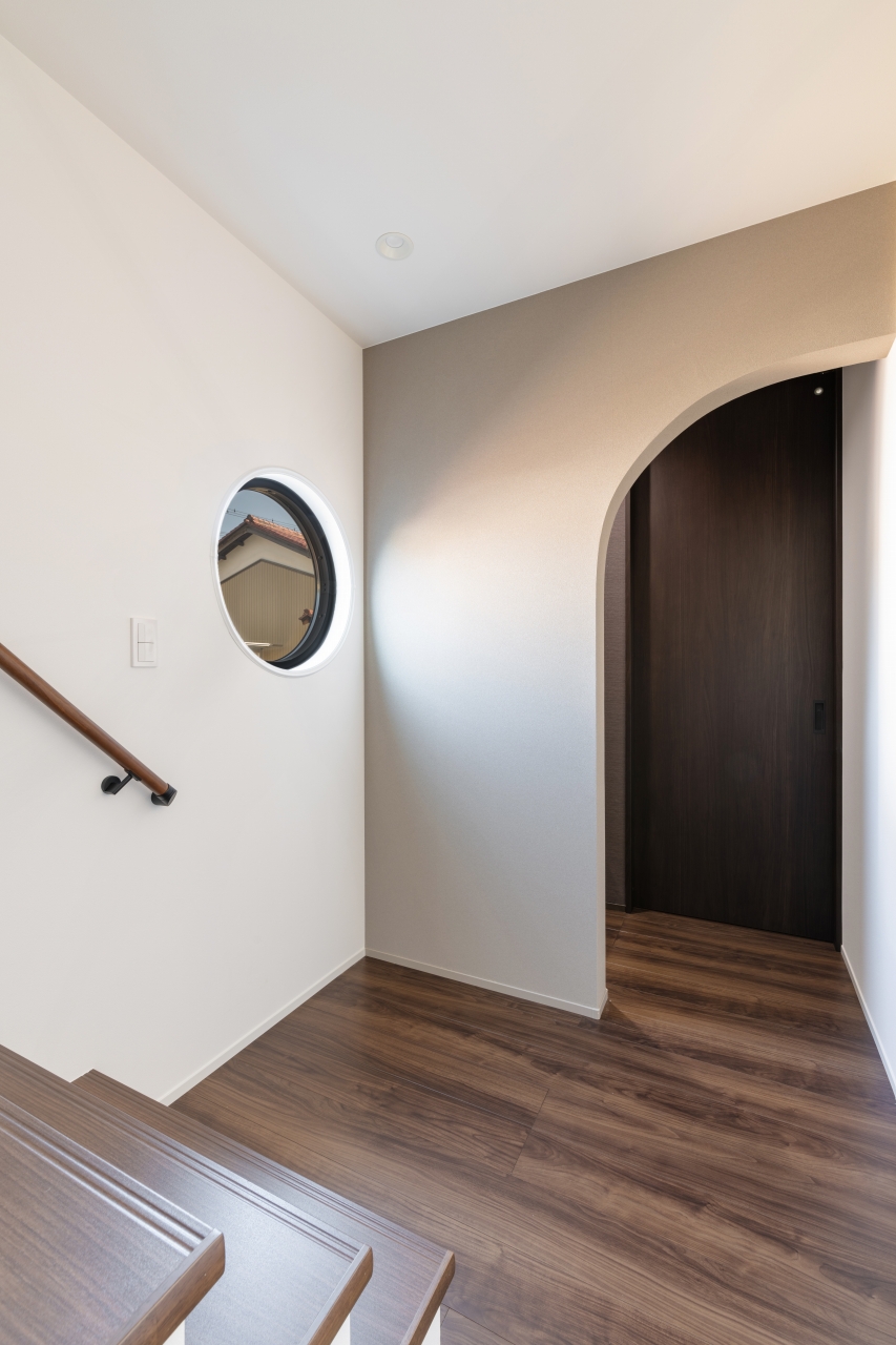 サンジョーホーム｜木目調のフローリングと丸窓が印象的な廊下。アーチ型のドア開口が空間に柔らかさを与えている。