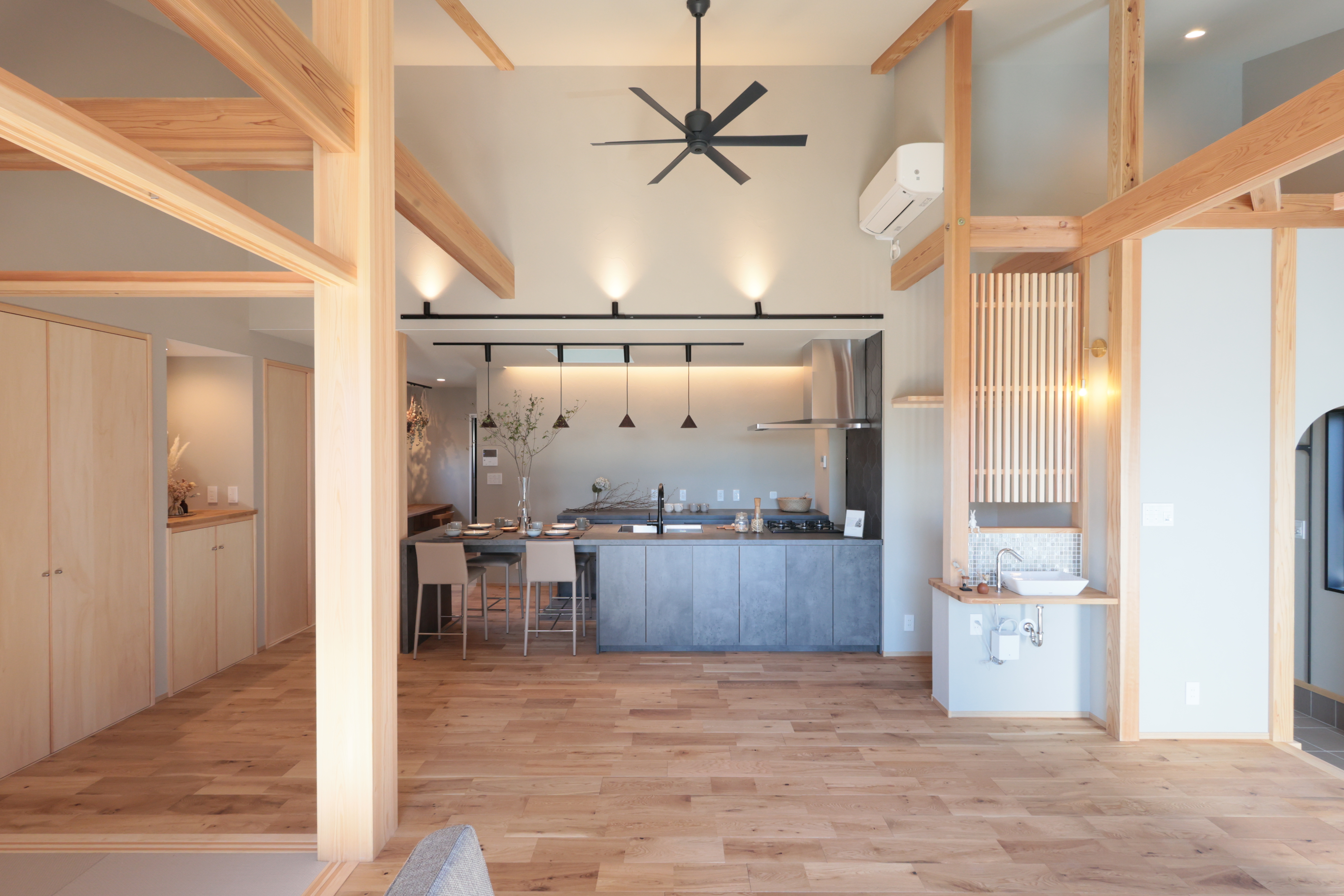 shiro’s（提坂工務店）【趣味、間取り、平屋】広々としたLDK空間は、木の温もりを感じさせる梁が印象的である。開放感のあるリビングとキッチンがシームレスにつながっており、家族でのくつろぎの時間を楽しめる。